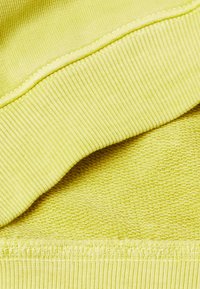Tessuto di cotone giallo con maglie lisce e testurizzate, con dettagli a coste lungo i bordi. La superficie presenta leggere variazioni di tonalità.