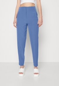 Ljusblå skräddarsydda byxor med hög midja, sidofickor och smalnade ben, tillverkade av ett mjukt tyg; stylat med vita plattformssandaler.