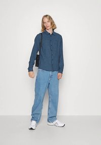 Plava karirana košulja s gumbima, svijetloplave široke traperice, bijele tenisice i mala crna torbica preko ramena. Jednostavan, ležeran outfit s kontrastnim teksturama.