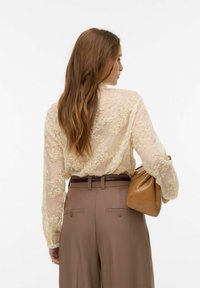 Kreemikas tikandiga lillemustriga pluus, läbipaistev materjal, pikad varrukad. Komplektis pruunid püksid ja beež käekott.