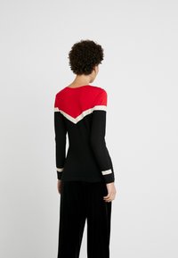 Langärmliges Oberteil in einem Farbdesign aus Rot, Schwarz und Weiß. Es verfügt über ein Chevron-Muster und eine figurbetonte Silhouette aus weichem Stoff.