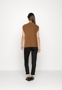 Wollen blend, bruine mouwloze top met ribbeltextuur; gecombineerd met zwarte, opgerolde broek en glanzende zwarte schoenen. Eenvoudig, gestructureerd ontwerp.