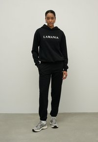 Juodas džemperis su užrašu "LAMANIA", derinamas su atitinkamais juodais sportiniais kelniais. Rinkinys pasižymi kasdiene siluetu ir tekstūruotu audiniu.