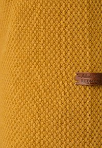 Strickstoff in leuchtendem Senfgelb mit strukturiertem, diagonalen Muster; verfügt über ein braunes Lederetikett mit der Prägung "Authentic Clothing REDMOND".
