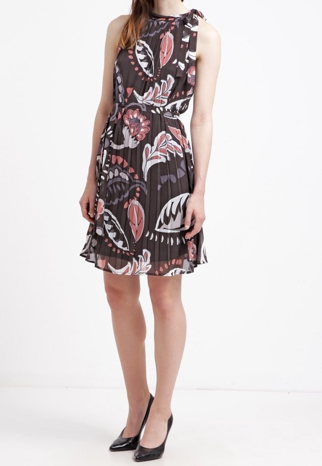 Femme portant une robe sans manches plissée avec un motif floral noir, blanc et rose, associée à des escarpins noirs à bout pointu.