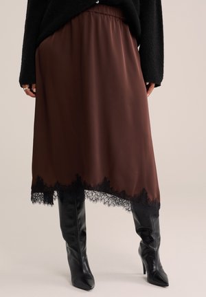 Gonna midi marrone con bordatura in pizzo nero, indossata con stivali neri alti al ginocchio con tacco e un maglione nero.