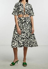 Set composto da un top corto a maniche corte e una gonna midi a fantasia bianco e nero, con un davanti annodato e sandali con tacco verde.
