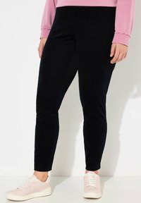 Svarta sammetstights med en figurnära design, som har en slät textur och en subtil lyster. Kombineras med ljusrosa sneakers.