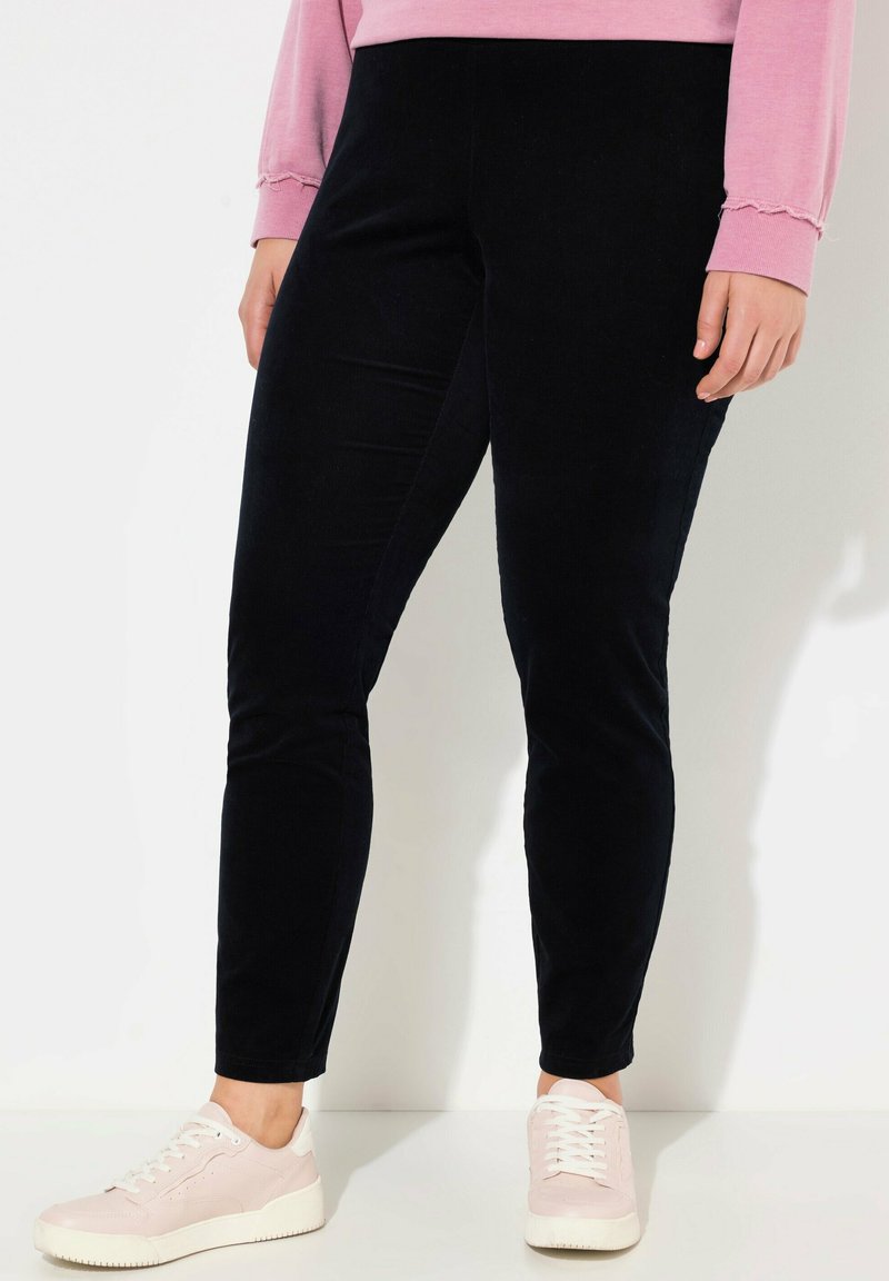 Svarta sammetstights med en figurnära design, som har en slät textur och en subtil lyster. Kombineras med ljusrosa sneakers.