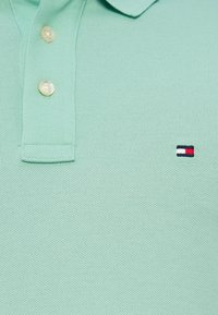 Πόλο μπλουζάκι από λεπτό πράσινο βαμβακερό πλεκτό ύφασμα με κλασικό γιακά. Διαθέτει τρία κουμπιά και μικρό κεντημένο λογότυπο σε ναυτικό μπλε, κόκκινο και λευκό.