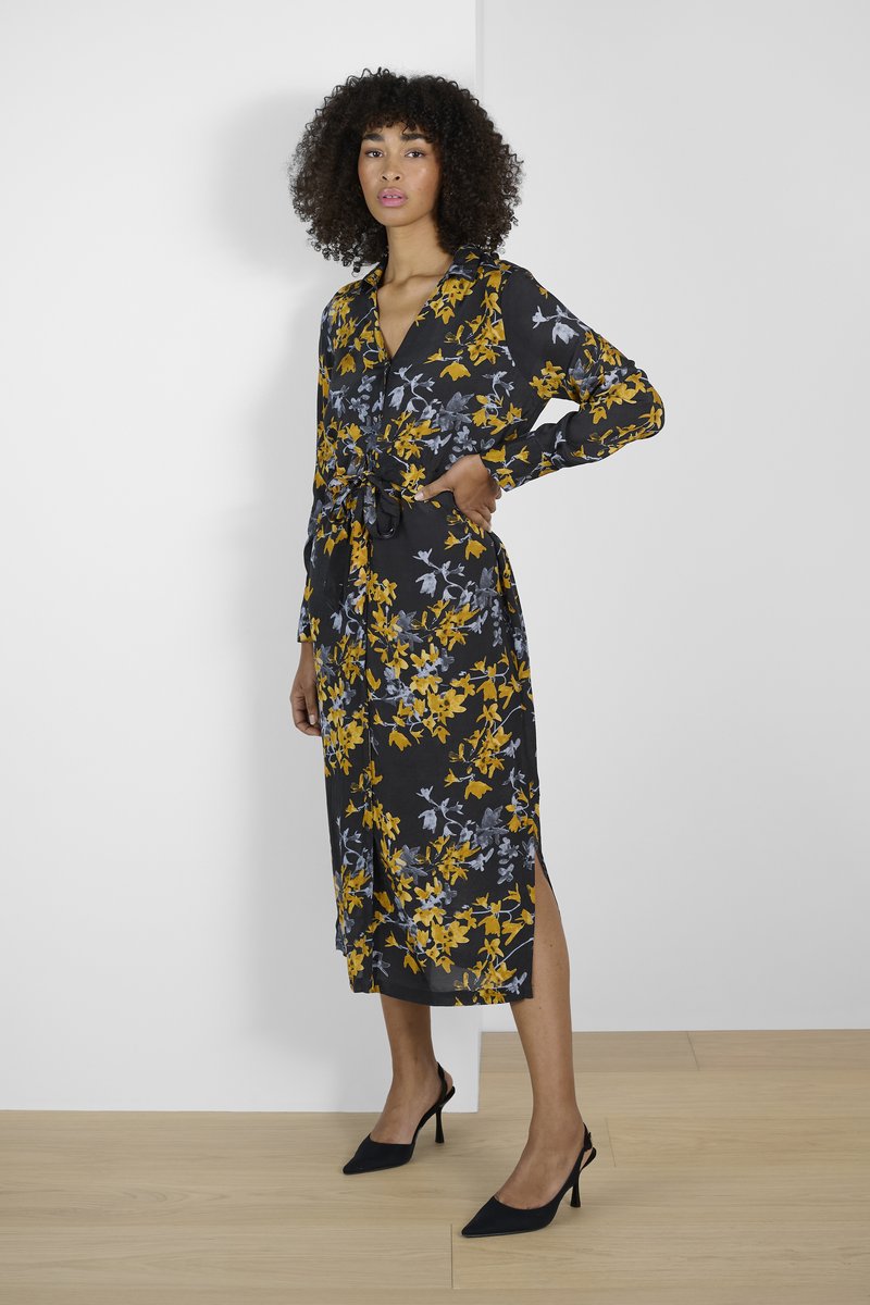 Black floral dress with yellow and grey patterns, long sleeves, a belted waist, and side slits. Paired with black high-heeled shoes.