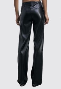 Pantaloni ampi in finta pelle nera con una texture liscia, vita alta e dettagli di cucitura minimali, mostrati da dietro.