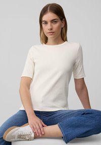 Haut blanc à manches courtes en côte avec un col rond, associé à un jean bleu cropped et des baskets blanches avec des accents beige.