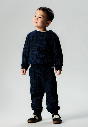 Chándal infantil azul marino con un diseño estampado, que incluye una sudadera de cuello redondo y pantalones con cintura elástica. Combinado con zapatillas negras.