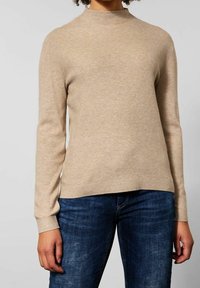 Beige långärmad tröja med hög halsringning, ribbade ärmslut och en något strukturerad yta. Matchas med mörkblå jeans.