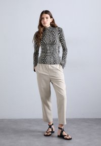 Maglietta a maniche lunghe a righe bianche e nere con colletto alto, abbinata a pantaloni beige cropped e sandali neri a pizzico. Tessuto liscio e aderente.