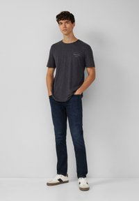 Ciemnoszara koszulka z krótkim rękawem o lekko fakturowanej powierzchni, w zestawie z ciemnoniebieskimi dżinsami i białymi trampkami z czarnymi akcentami. Swobodny strój.