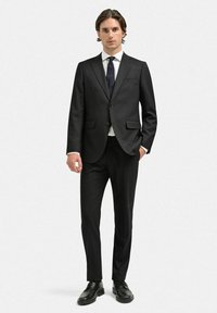 Svart skräddarsydd kostym med en knappjacka, vit skjorta och blått slips. Har glatt tyg och slim-fit design, ihop med svarta skor.