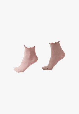 Paire de chaussettes chevilles côtelées rose clair avec bords à volants présentées sur des modèles de pieds invisibles.