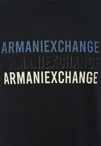 Svart bomull T-skjorte med stablet "ARMANIEXCHANGE" tekst i blå, svart og hvit, med varierende skrifttyper og størrelser. Klassisk crew neck design.