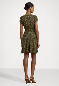 Abito floreale verde con maniche a sbuffo corte, vita regolabile con un nodo e gonna a campana. Presenta una zip sul retro e motivi floreali intricati in vari colori.