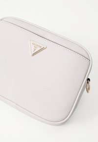 Clutch in pelle grigia chiara con una texture liscia e accessori triangolari in oro con il logo del marchio. Chiusura con zip e dettaglio in metallo a forma di anello.