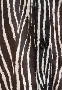 Černobílé pruhované tkaniny s vertikálními, nerovnými liniemi, s černým knoflíkem viditelným vpravo uprostřed. Texturovaný povrch.