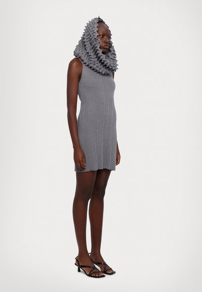 Graues geripptes Kleid mit hohem Kragen und Rüschenschal-Haaraccessoire, kombiniert mit schwarzen Sandalen mit Riemen, vor einem neutralen Hintergrund präsentiert.