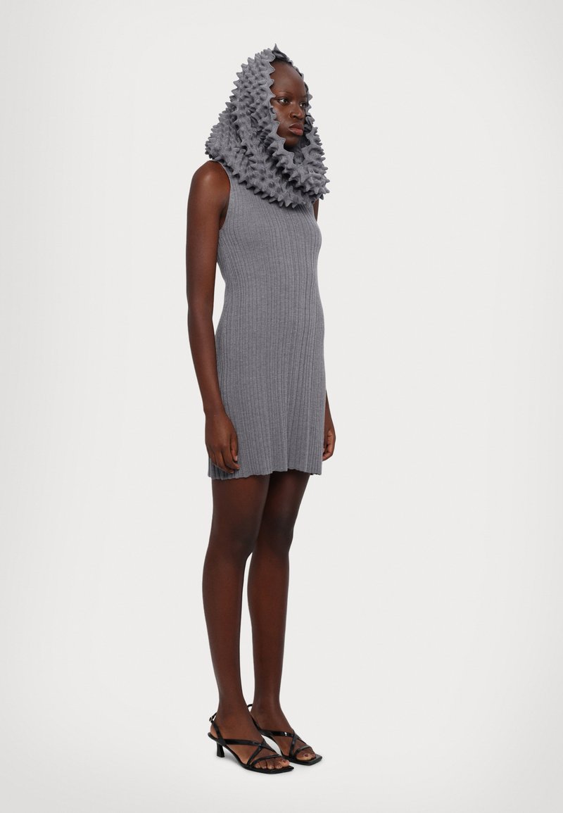 Abito grigio a costine con collo alto e copricapo di sciarpa arricciata, abbinato a sandali neri con cinturini, esposto su uno sfondo neutro.