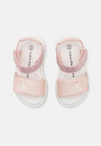 Rosa sandaler med justerbare stropper, hvite såler og "cK"-logo på en fremre stropp. Glatt materiale, rund form og polstrede innersåler.