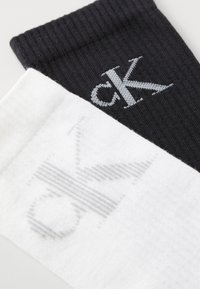 Sokker i en bomuldsblanding i sort og hvid, med ribbet design og et logo i kontrasterende farver på hver sok.