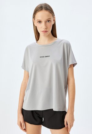 Graues, kurzärmeliges Sportoberteil mit Netzstruktur und dem Text "GOOD ENERGY". Lockere Passform, runder Ausschnitt. Kombiniert mit schwarzen Shorts.