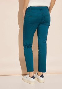 Úzké tyrkysové kalhoty z elastické látky, které mají dvě zadní kapsy, boční švy a hladkou texturu. Nosit je s bílými teniskami.