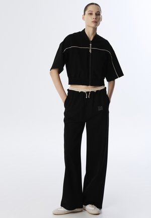Giacca nera corta con zip frontale e dettagli in crema, abbinata a pantaloni neri con vita elastica e ricamo. Tessuto leggero.