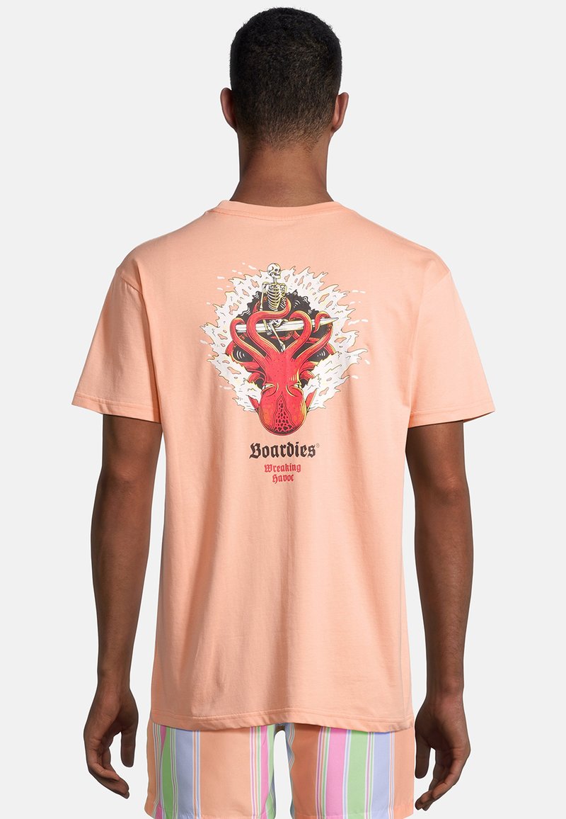 Camiseta de algodón color durazno con un estampado gráfico de un pulpo rojo y un esqueleto en la parte posterior. Tienen mangas cortas, un corte relajado y un diseño de cuello redondo.