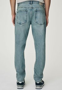 Jean bleu clair avec une coupe droite, doté de deux poches arrière, de coutures visibles et d'une texture en denim douce.