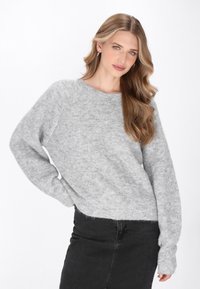 Pulover texturat de culoare gri deschis, cu guler rotund și mâneci raglan, asociat cu o fustă neagră, pe un fundal alb simplu.