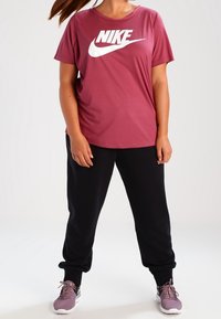 Bordová krátká rukávová tričko Nike s velkým bílým logem. V kombinaci s černými joggingovými kalhotami a šedými sportovními botami.
