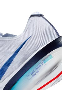 Hvid løbesko med struktureret overdel, blå swoosh-detalje, kontrasterende navy hælkappe og lyseblå sål med røde accenter og mærkning.