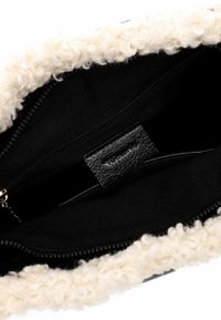 Interno di una borsa in pelle nera con un bordo in tessuto bianco morbido e peloso. Presenta una cerniera liscia e un'etichetta nera visibile all'interno.