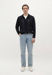 Cămașă albastru marin cu nasturi și dungi verticale texturate, asortată cu blugi de denim albastru deschis și adidași albi. Design simplu, cu o croială relaxată.