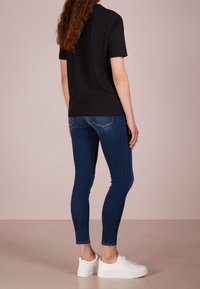 Camiseta negra de manga corta, vaqueros ajustados azules y zapatillas blancas. Tejido suave, corte informal, color sólido, vaqueros de longitud tobillo con bolsillos traseros.