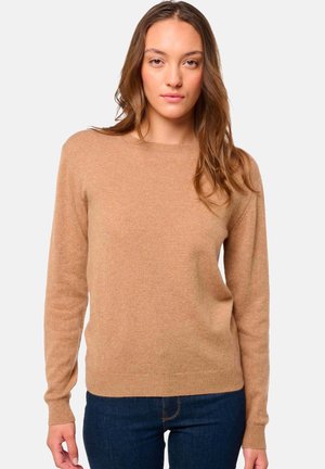 Pull en maille beige à manches longues, col rond et poignets et ourlet côtelés. Porté avec un jean noir. Texture lisse, coupe décontractée.