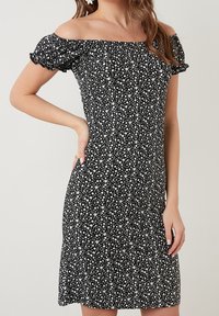 Sort off-shoulder kjole med hvidt blomster mønster. Korte flæsermer, tætsiddende silhuet og lårkort længde. Blød stofstruktur.