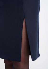 Námořnická sukně s texturovanou tkaninou, která má boční rozparek a hladký lem. Vnitřní podšívka je světlejší odtín viditelný na rozparku.