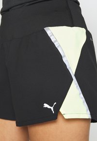 Black athletic shorts featuring a yellow accent panel, silver trim, and a white logo. Smooth fabric, mid-rise waistband, and relaxed fit.