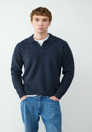 Marineblauwe, langmouwige poloshirttrui met een gestructureerde brei, drie-knops sluiting en geribde manchetten, gedragen over een wit T-shirt en blauwe jeans.