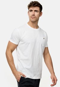 Hvid crew-neck t-shirt lavet af letvægtsstof, med korte ærmer og en lille brystlomme med knapdetalje.