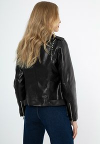 Giubbotto da moto in pelle nera con colletto a scatto, borchie argentate lungo le cuciture delle spalle e polsini con zip per una vestibilità regolabile.