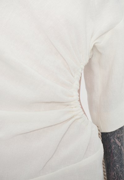 White linen top featuring gathered ruching at the waist, short sleeves, and a soft texture. The fabric has a light, slightly sheer appearance.